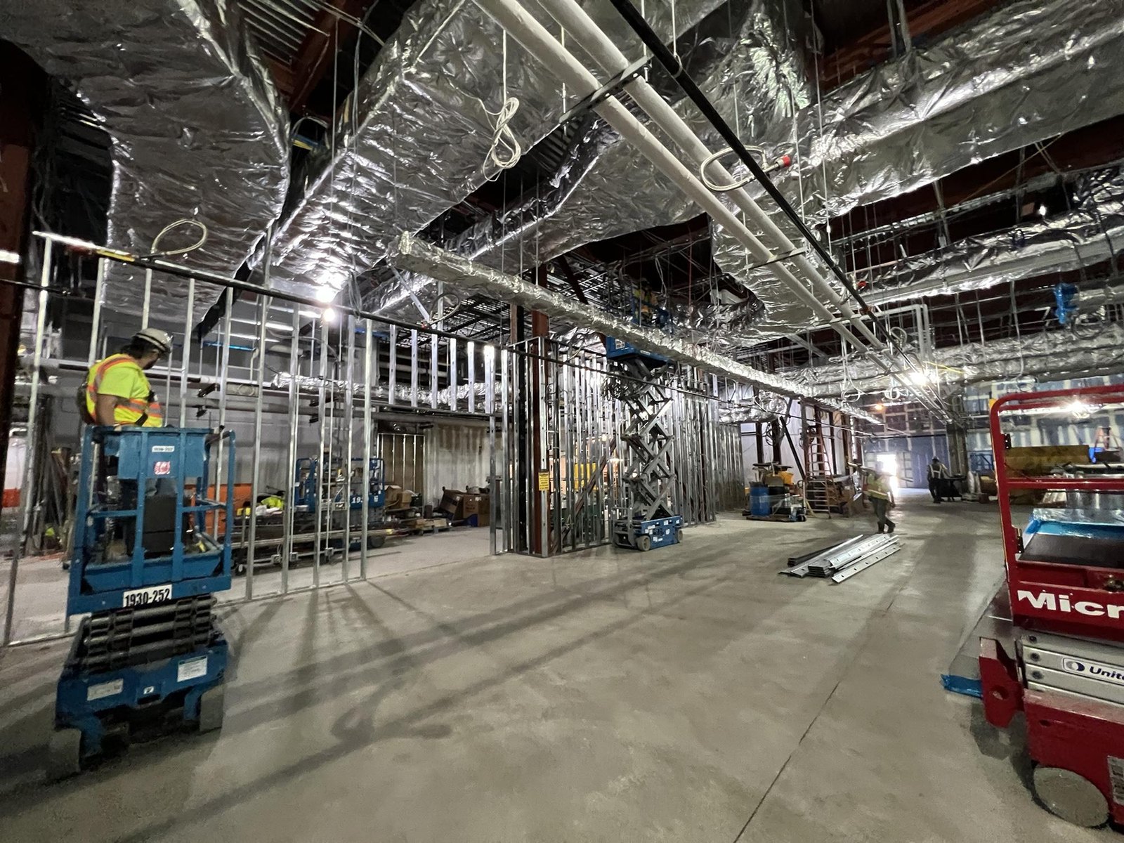 Commercial interior buildout with exposed ductwork, metal framing, and construction crews