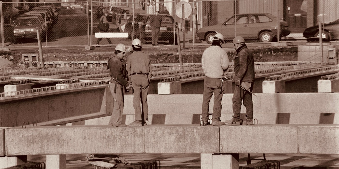Four construction workers conferring among concrete beams and reinforcing steel