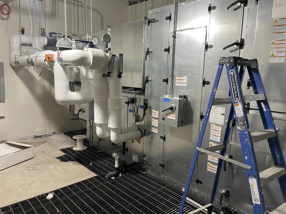 Mechanical equipment room with insulated piping, air handling equipment, and a ladder